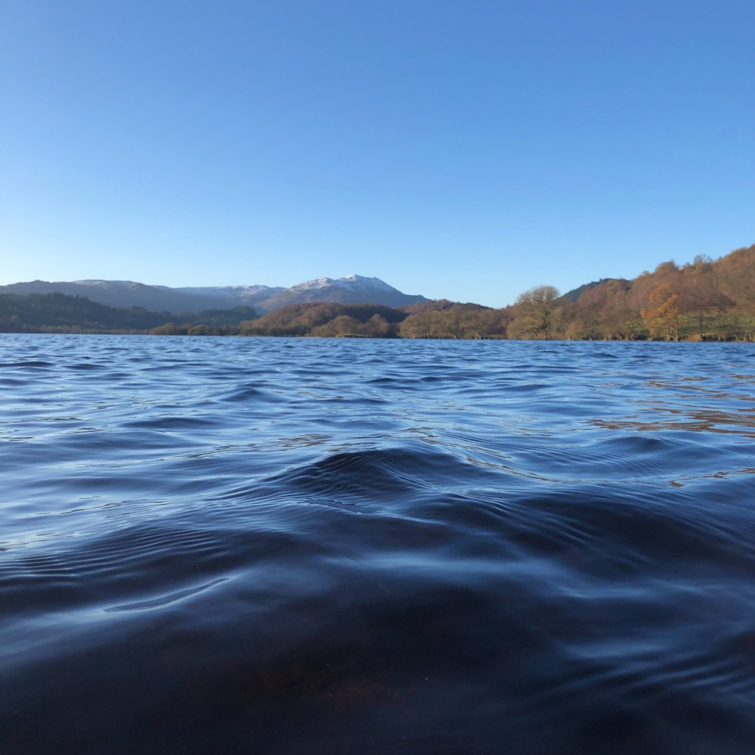 Calm lake surface with mountains and clear blue sky in the background.
