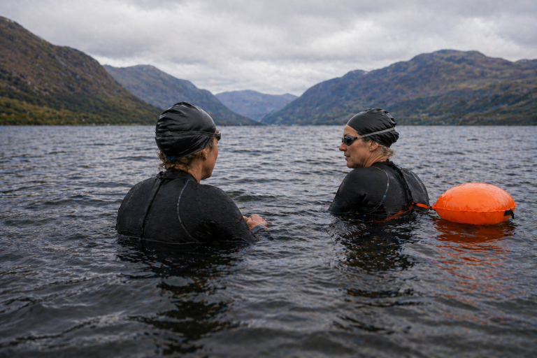 Open water swimming coach supporting beginner swimmer Open water swimming coach speaking with a beginner swimmer in a Scottish loch during a 1:1 coaching session